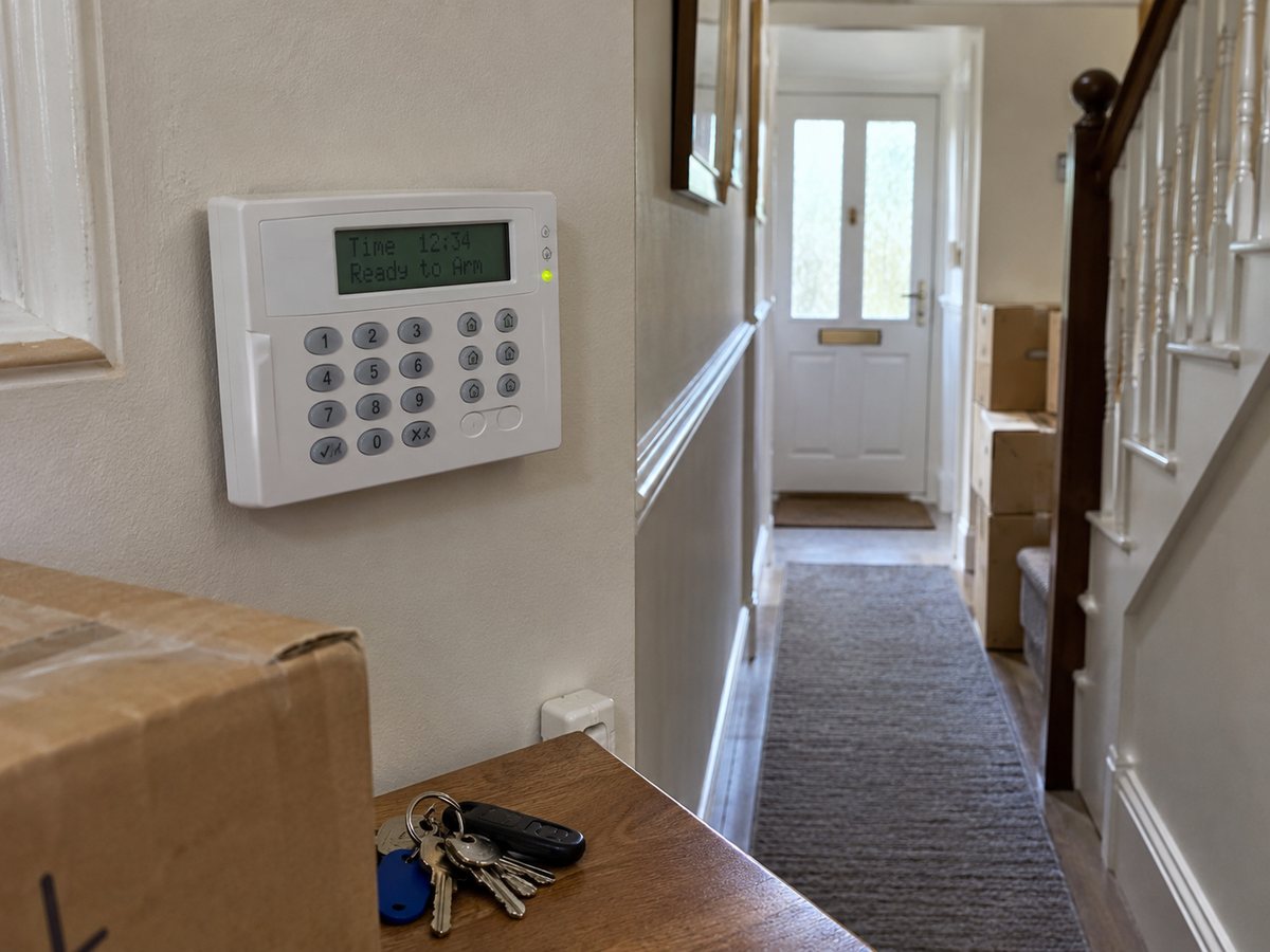 Burglar alarm keypad in the hallway of a house with moving boxes and keys